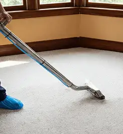 Steam carpet cleaning technician using a hot-water extraction wand on a residential carpet, wearing blue protective shoe covers Boise, ID.